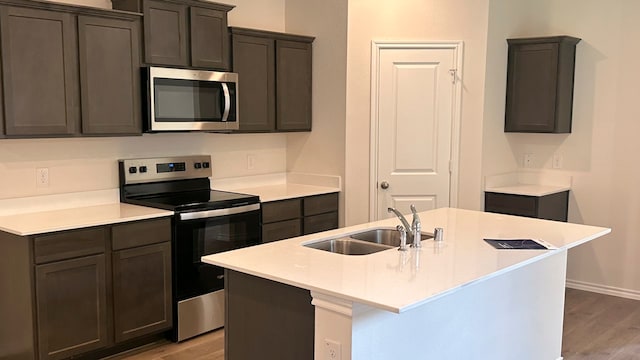 kitchen with sink, appliances with stainless steel finishes, light hardwood / wood-style flooring, and an island with sink