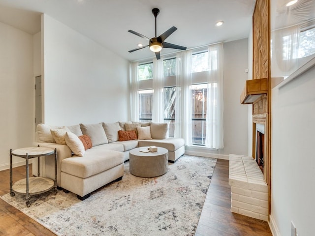 living room featuring ceiling fan, a high ceiling, dark hardwood / wood-style floors, and a brick fireplace