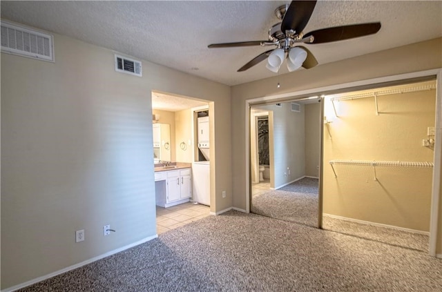 unfurnished bedroom featuring a closet, ensuite bath, light tile patterned floors, a textured ceiling, and ceiling fan