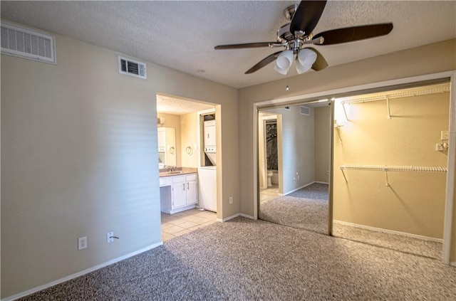 unfurnished bedroom featuring ensuite bath, sink, light colored carpet, ceiling fan, and a textured ceiling