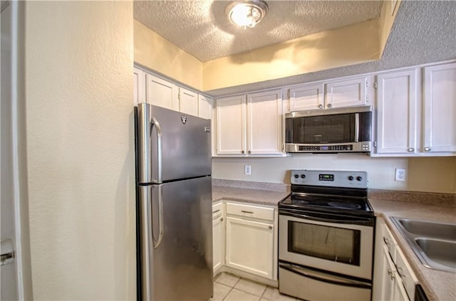 kitchen featuring appliances with stainless steel finishes, a textured ceiling, white cabinets, and light tile patterned floors