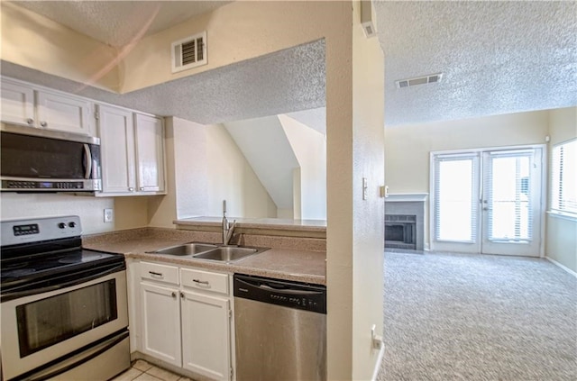 kitchen featuring stainless steel appliances, white cabinets, sink, a textured ceiling, and light carpet