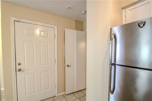 kitchen with a textured ceiling, stainless steel refrigerator, white cabinets, and light tile patterned floors