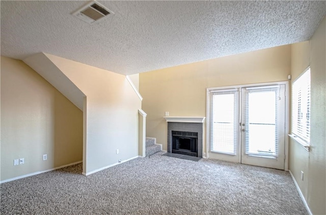 unfurnished living room featuring carpet, a tiled fireplace, and a textured ceiling