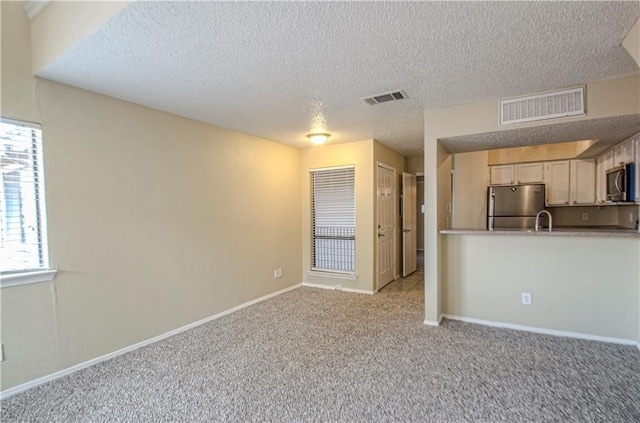 unfurnished living room with light carpet, sink, and a textured ceiling