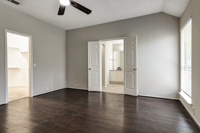 unfurnished bedroom featuring ensuite bath, lofted ceiling, dark hardwood / wood-style flooring, ceiling fan, and a textured ceiling