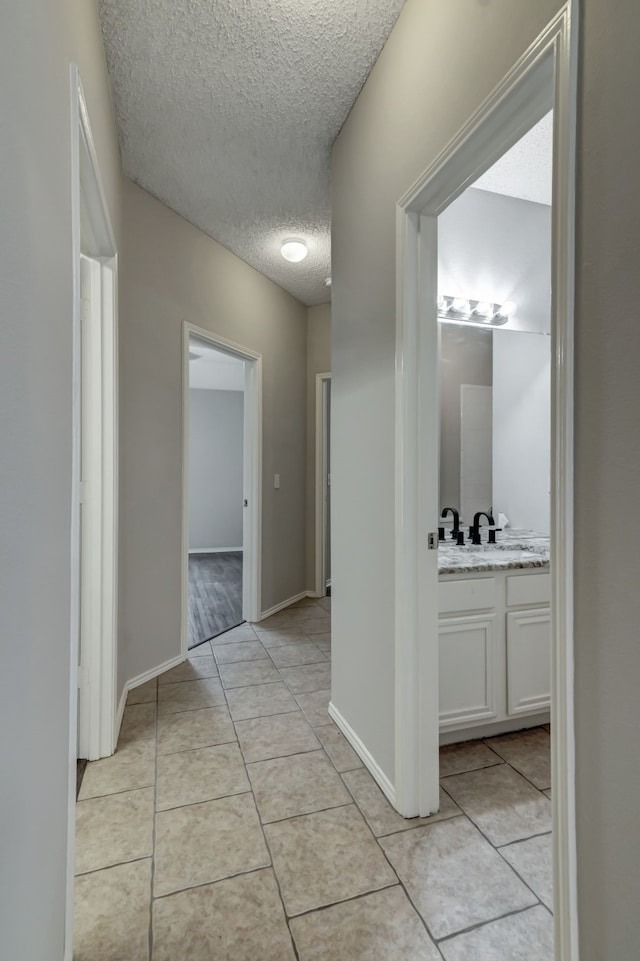 corridor featuring sink, light tile patterned floors, and a textured ceiling