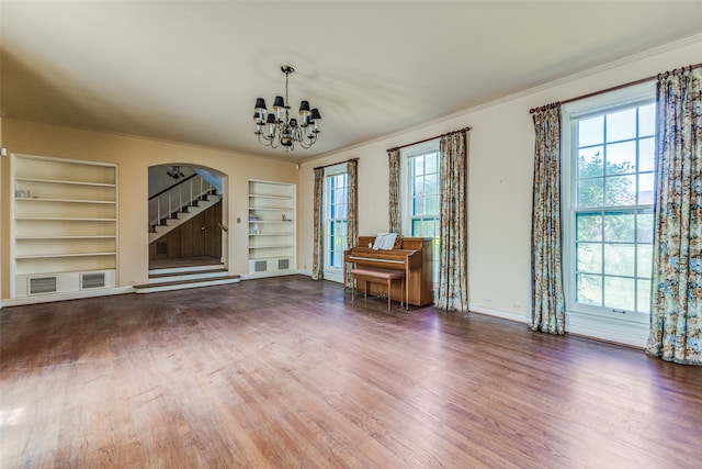 unfurnished living room featuring dark hardwood / wood-style floors, built in shelves, and an inviting chandelier