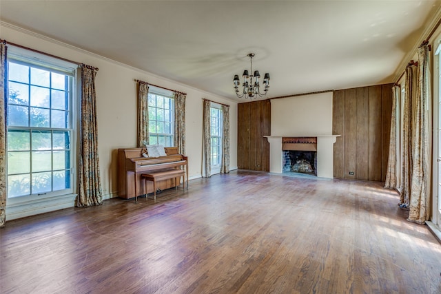 unfurnished living room featuring wooden walls, crown molding, hardwood / wood-style floors, and a chandelier