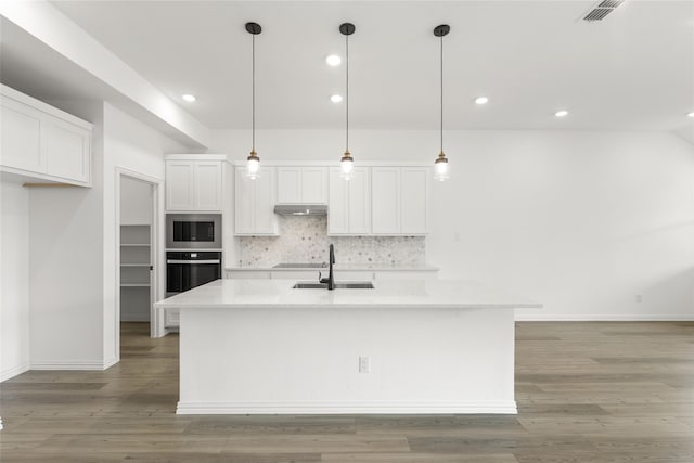 kitchen with a kitchen island with sink, white cabinets, built in microwave, and stainless steel oven