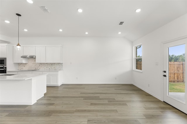 kitchen featuring stainless steel microwave, tasteful backsplash, white cabinets, decorative light fixtures, and vaulted ceiling