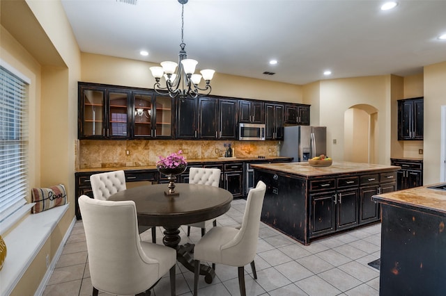 kitchen featuring pendant lighting, backsplash, appliances with stainless steel finishes, dark brown cabinets, and a kitchen island