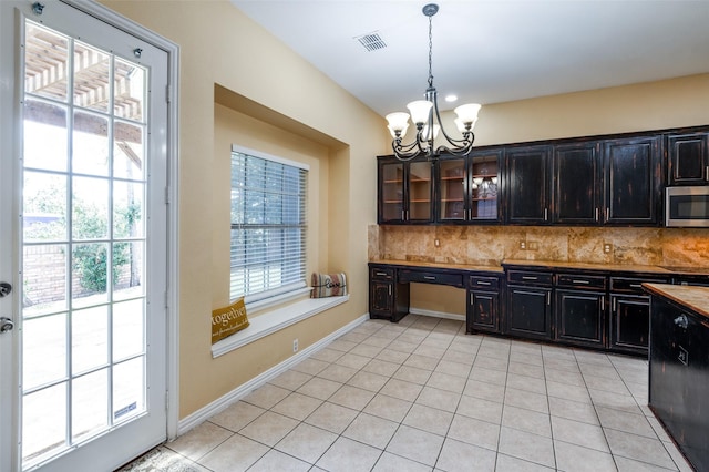 kitchen featuring tasteful backsplash, dark brown cabinetry, an inviting chandelier, hanging light fixtures, and light tile patterned flooring