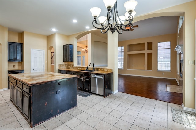 kitchen featuring wooden counters, an inviting chandelier, sink, stainless steel dishwasher, and a kitchen island