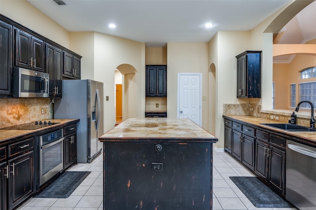 kitchen with decorative backsplash, appliances with stainless steel finishes, sink, light tile patterned floors, and a center island