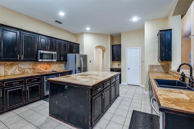 kitchen featuring a center island, backsplash, sink, light tile patterned floors, and stainless steel appliances