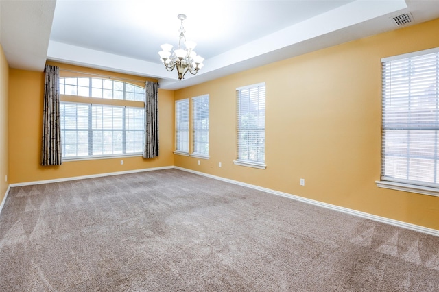 empty room with a chandelier, carpet floors, and a raised ceiling