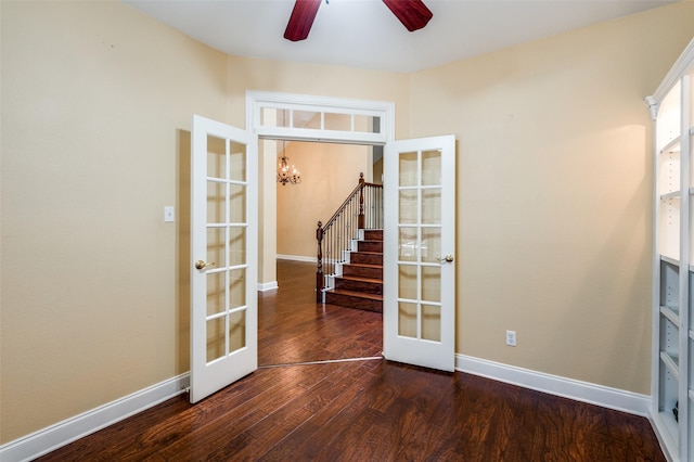 spare room featuring dark hardwood / wood-style floors, ceiling fan with notable chandelier, and french doors