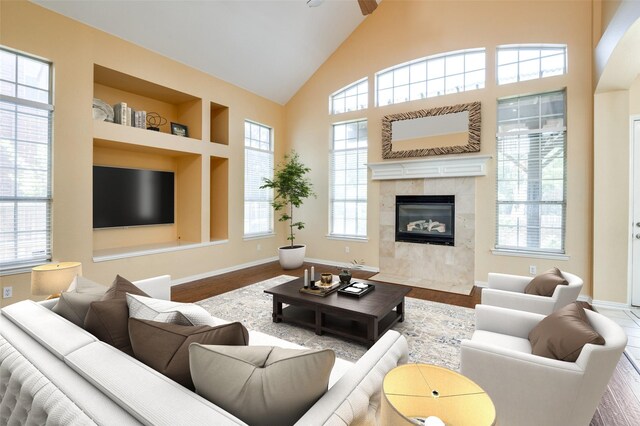 living room with a tile fireplace, ceiling fan, built in features, and hardwood / wood-style flooring