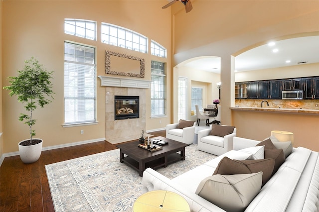 living room featuring plenty of natural light, ceiling fan, dark wood-type flooring, and a tiled fireplace