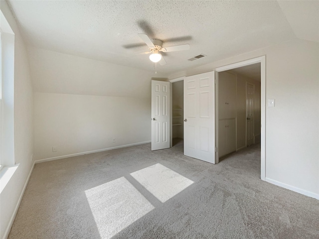 unfurnished bedroom featuring visible vents, light carpet, vaulted ceiling, a textured ceiling, and baseboards