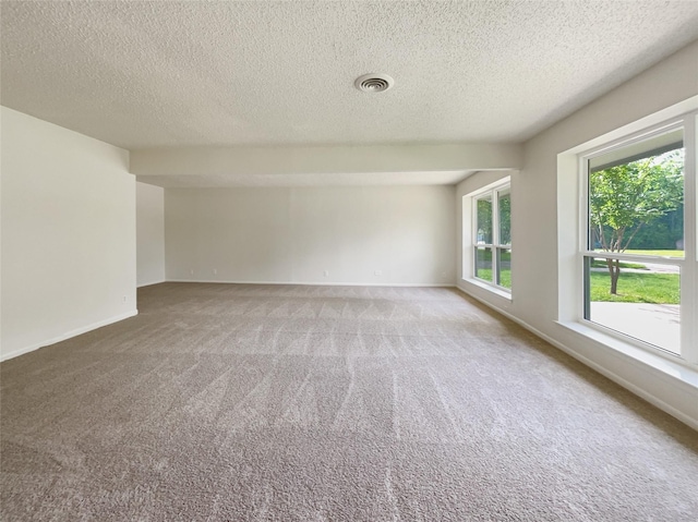 carpeted empty room featuring visible vents, a textured ceiling, and baseboards