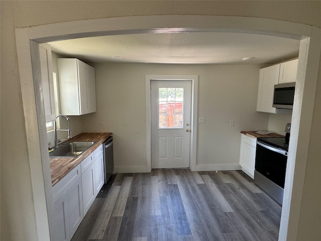 kitchen with wooden counters, sink, dark hardwood / wood-style floors, white cabinetry, and stainless steel appliances