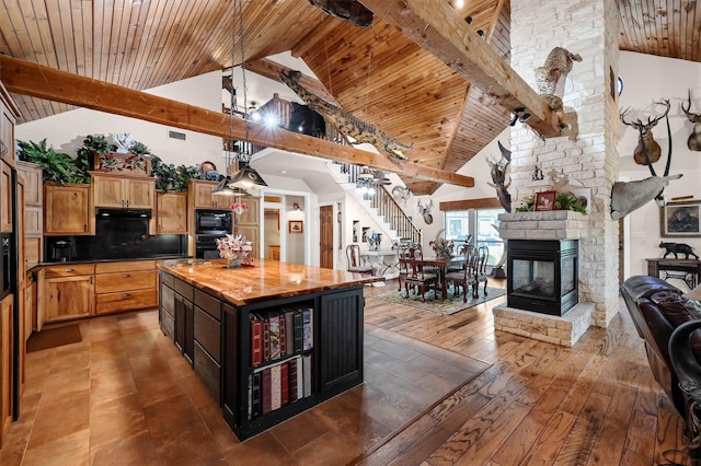 kitchen featuring black appliances, a stone fireplace, a center island, dark hardwood / wood-style flooring, and high vaulted ceiling