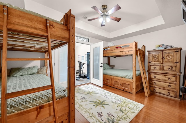 bedroom with ceiling fan, a tray ceiling, and hardwood / wood-style flooring