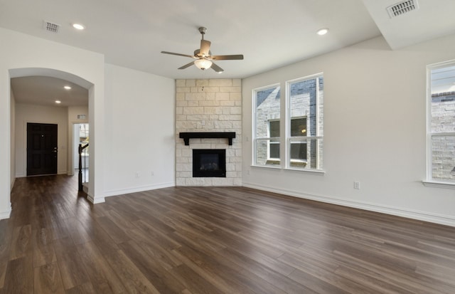 unfurnished living room featuring ceiling fan, dark hardwood / wood-style floors, and a stone fireplace