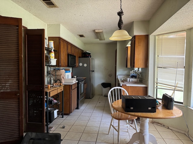 kitchen with a textured ceiling, light tile patterned floors, hanging light fixtures, and appliances with stainless steel finishes