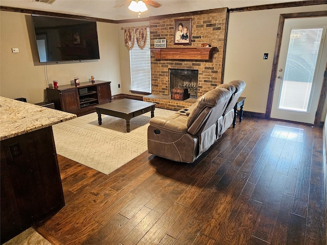 living room featuring dark wood-type flooring, ceiling fan, crown molding, and a brick fireplace