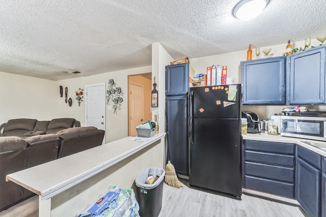 kitchen featuring stainless steel microwave, light countertops, freestanding refrigerator, and blue cabinets
