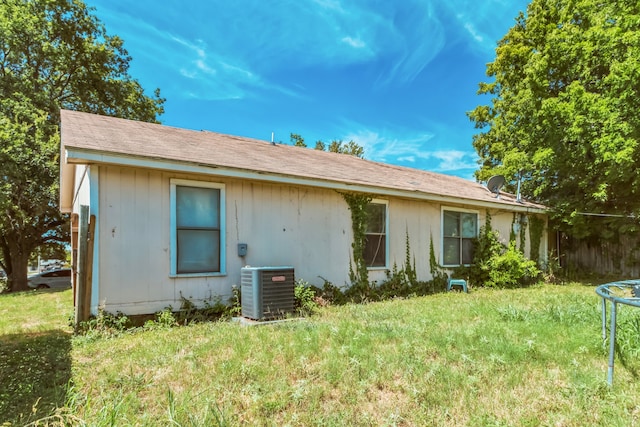 rear view of property with a trampoline, central air condition unit, and a yard