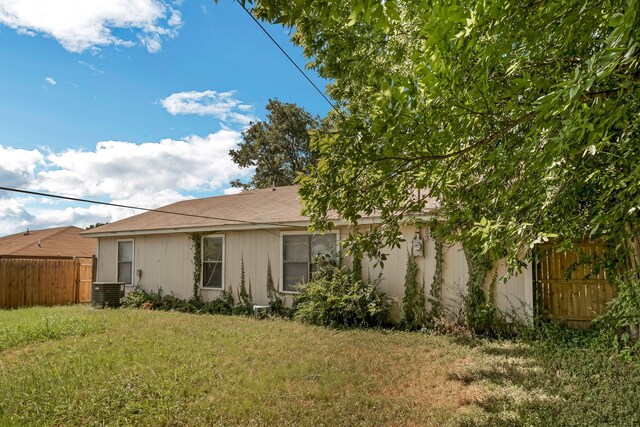 rear view of property with central air condition unit and a yard