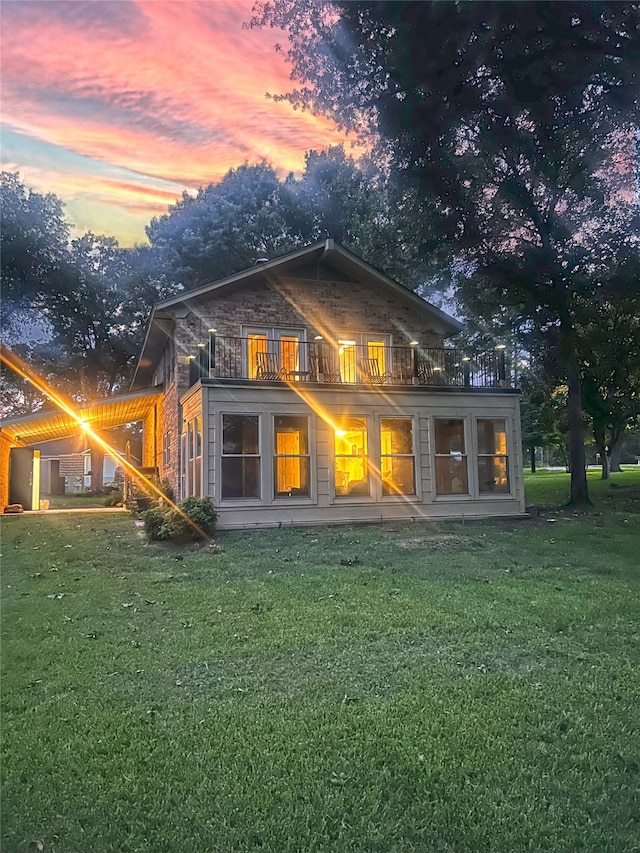 back house at dusk with a balcony and a lawn