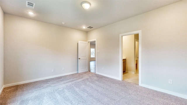 unfurnished bedroom with baseboards, ensuite bath, visible vents, and light colored carpet