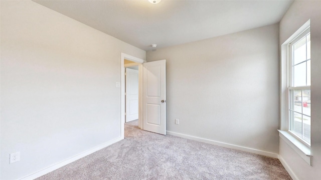 spare room with baseboards, plenty of natural light, and light colored carpet