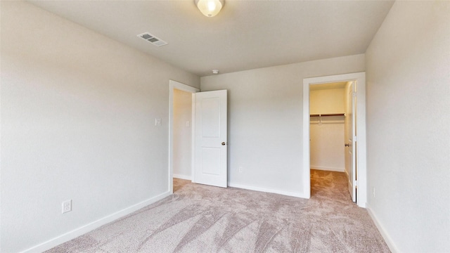 unfurnished bedroom with carpet flooring, a walk in closet, visible vents, and baseboards