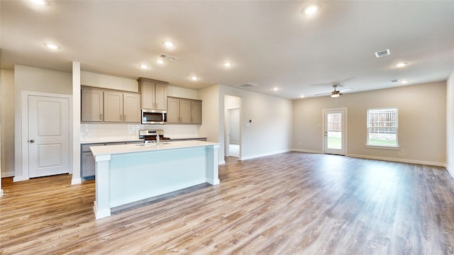 kitchen with appliances with stainless steel finishes, light hardwood / wood-style floors, ceiling fan, and a center island with sink