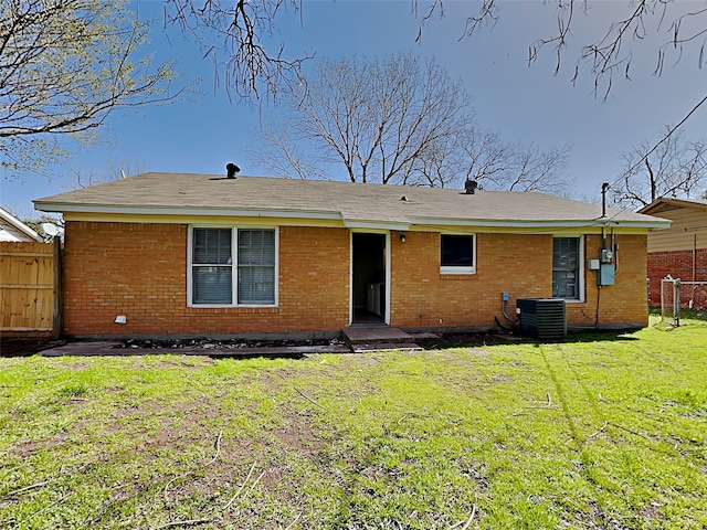 rear view of house featuring central AC, fence, brick siding, and a lawn