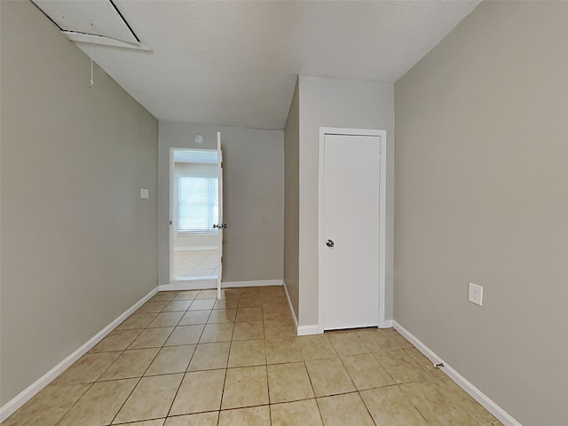 spare room featuring attic access, baseboards, a textured ceiling, and light tile patterned flooring