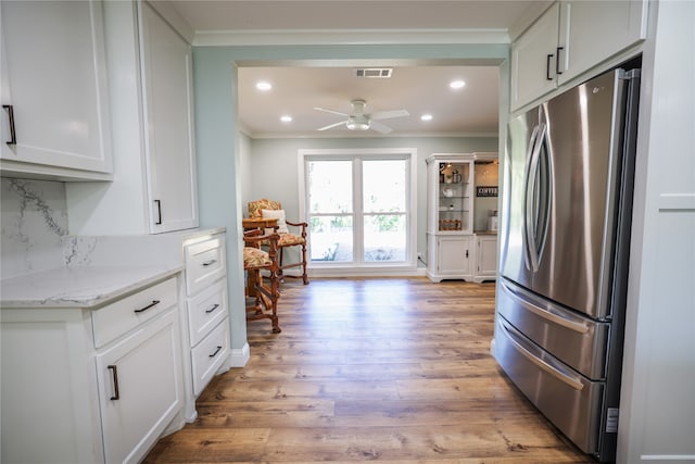 kitchen featuring tasteful backsplash, stainless steel refrigerator, ornamental molding, white cabinets, and light stone counters