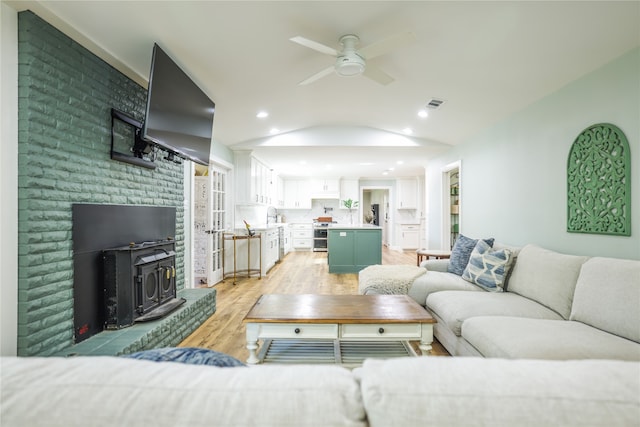 living room with ceiling fan, vaulted ceiling, light hardwood / wood-style floors, sink, and a wood stove