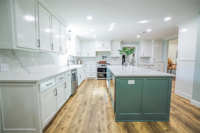 kitchen featuring white cabinets, a center island, stainless steel appliances, light wood-type flooring, and light stone counters