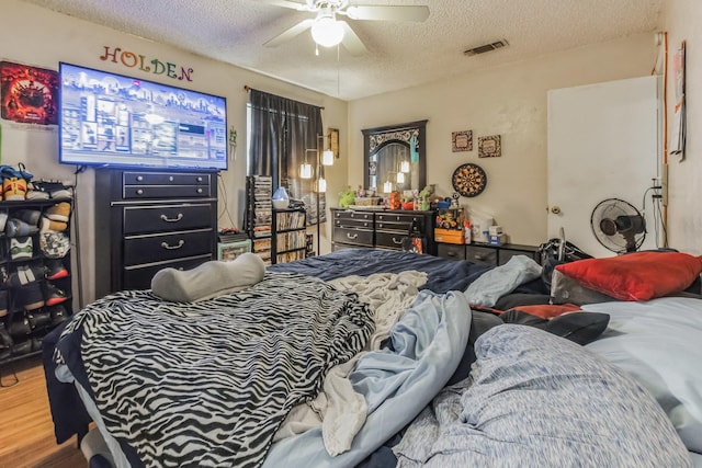 bedroom with a textured ceiling, wood finished floors, visible vents, and a ceiling fan