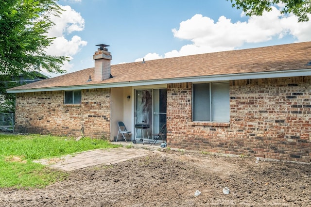 back of house with a patio area, roof with shingles, a chimney, and brick siding