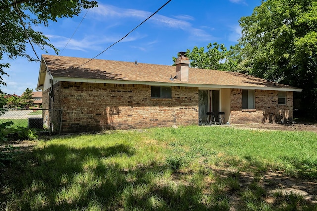 rear view of house with brick siding, a chimney, fence, and a lawn