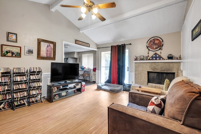 living room featuring wood-type flooring, a brick fireplace, ceiling fan, and vaulted ceiling with beams