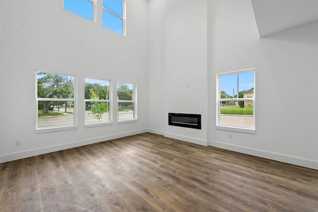 unfurnished living room featuring wood-type flooring, a wealth of natural light, and a towering ceiling